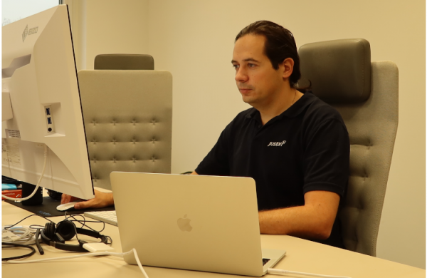Ein Mann, der ein schwarzes T-Shirt trägt, sitzt an einem Schreibtisch und arbeitet an einem Computer.