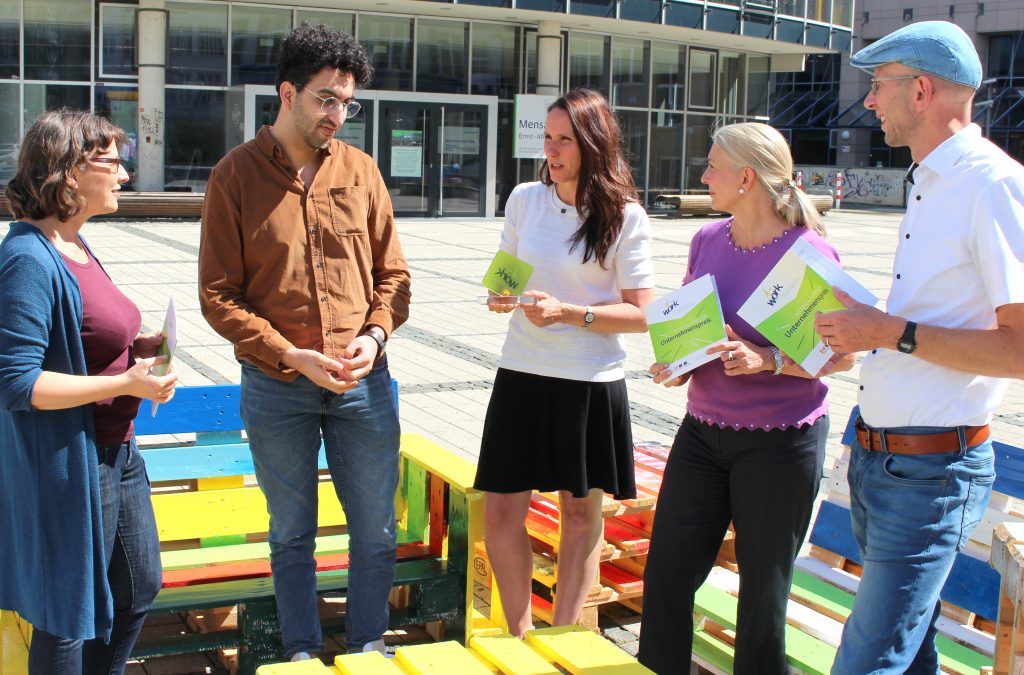Five people in conversation. In the background a colourful bench.