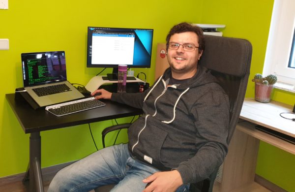 Mann sitzt in Bürostuhl dem Betrachter zugewandt, im Hintergund Lapto, Tastatur und Bildschirm auf einem Schreibtisch