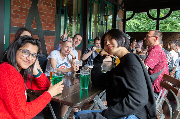 Gruppe von etwa 10 Personen sitzen an einem Tisch, auf dem Getränke stehen, Personen blicken in Kamera