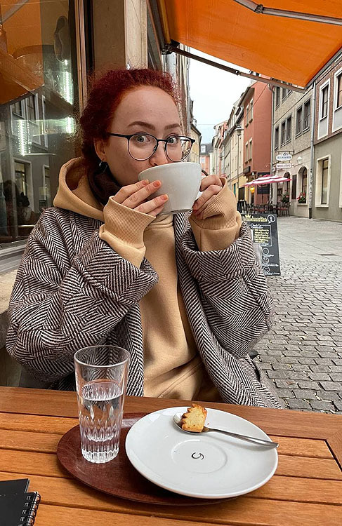 Eine junge Frau sitzt im Straßencafé und hält eine Tasse.