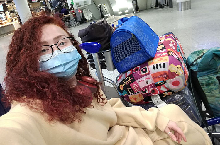 Eine junge Frau mit Mund-Nase-Bedeckung sitzt mit einem Kofferwagen neben sich.