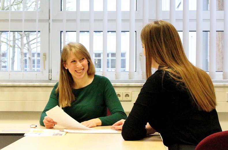 Two smiling women sit at the table in a counselling situation.