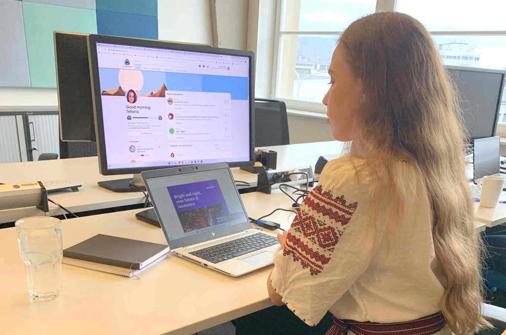 Eine junge Frau sitzt am Schreibtisch vor Laptop und Monitor.