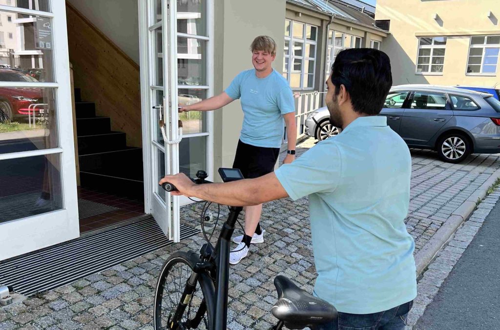 Eine Person öffnet einer anderen Person mit Fahrrad die Tür zu einem Gebäude.