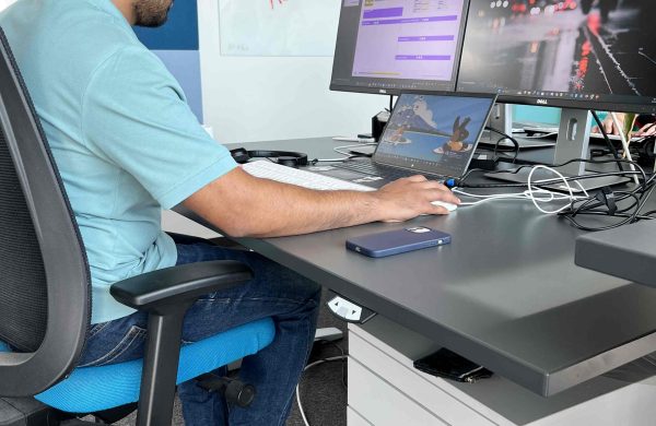 Eine Person sitzt am Schreibtisch vor Monitoren.