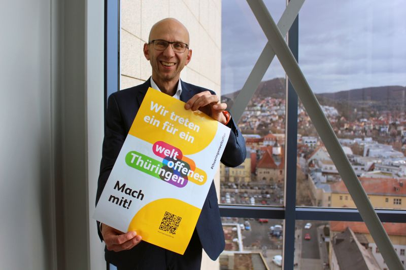 Mann hält Plakat der Kampagne Weltoffenes Thüringen in die Kamera und lacht.